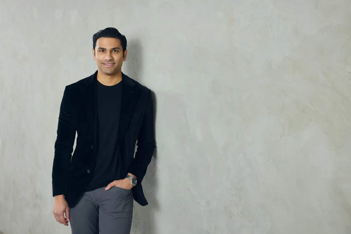 A well-dressed man leans against a neutral colored wall