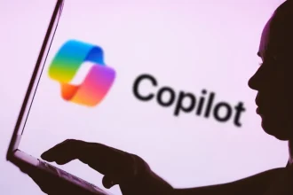 In this photo illustration, the Microsoft Copilot logo is seen in the background next to a silhouette of a person using a notebook.