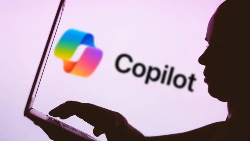 In this photo illustration, the Microsoft Copilot logo is seen in the background next to a silhouette of a person using a notebook.