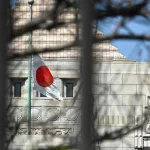 a Japanese flag fluttering in the wind in the distance in front of a building in Tokyo